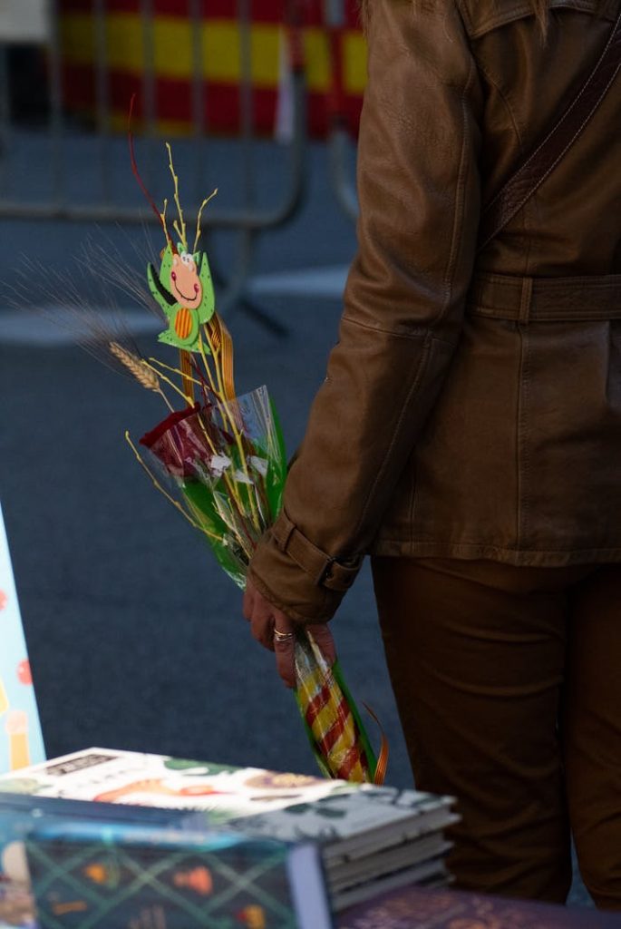 Person in brown jacket holding a red rose at a Sant Jordi festival street market.