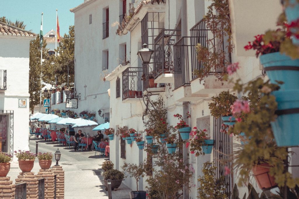 Charming Mediterranean street with outdoor cafes, balconies, and vibrant flowers in pots.